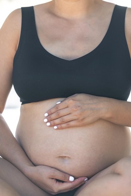 Pregnant woman touches big belly while sitting on bed