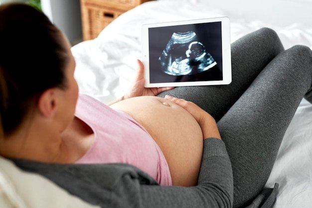 Pregnant woman watching at ultrasound record on tablet