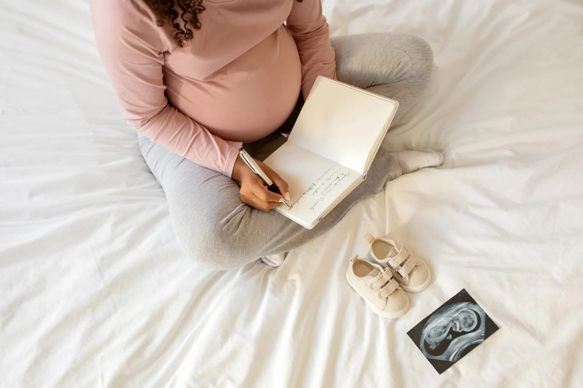 Pregnant woman writing down thoughts in her notebook at home