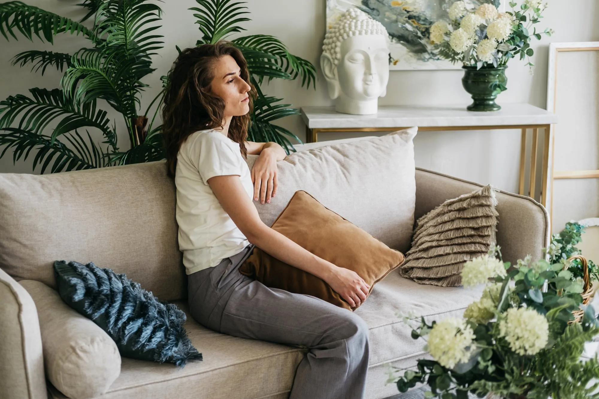 A sad woman sits on a sofa at home hugging a pillow