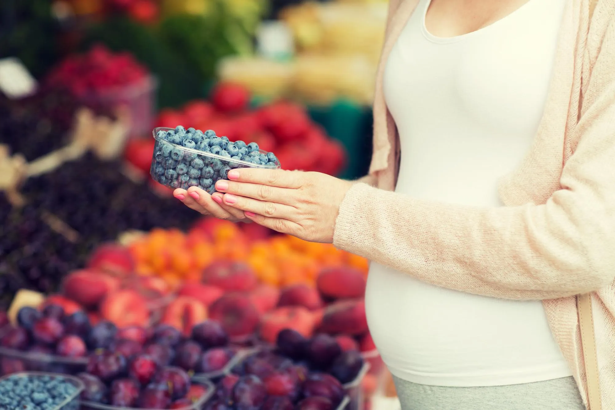 sale, shopping, pregnancy and people concept - close up of pregnant woman choosing blueberries at street food market