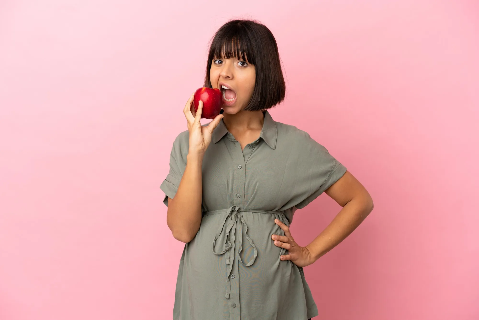 Woman over isolated background pregnant and holding an apple