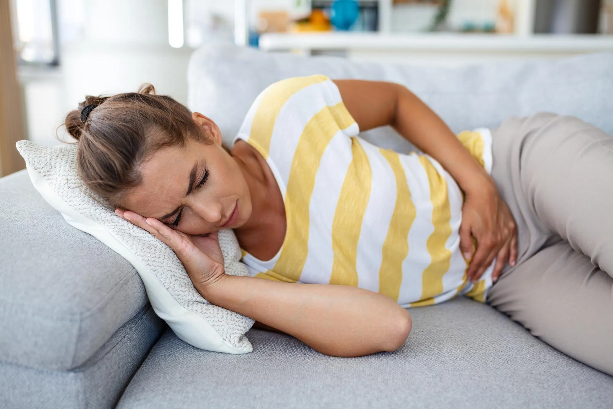 Woman lying on sofa looking sick in the living room Beautiful young woman lying on bed and holding hands on her stomach Woman having painful stomachache on bed Menstrual period