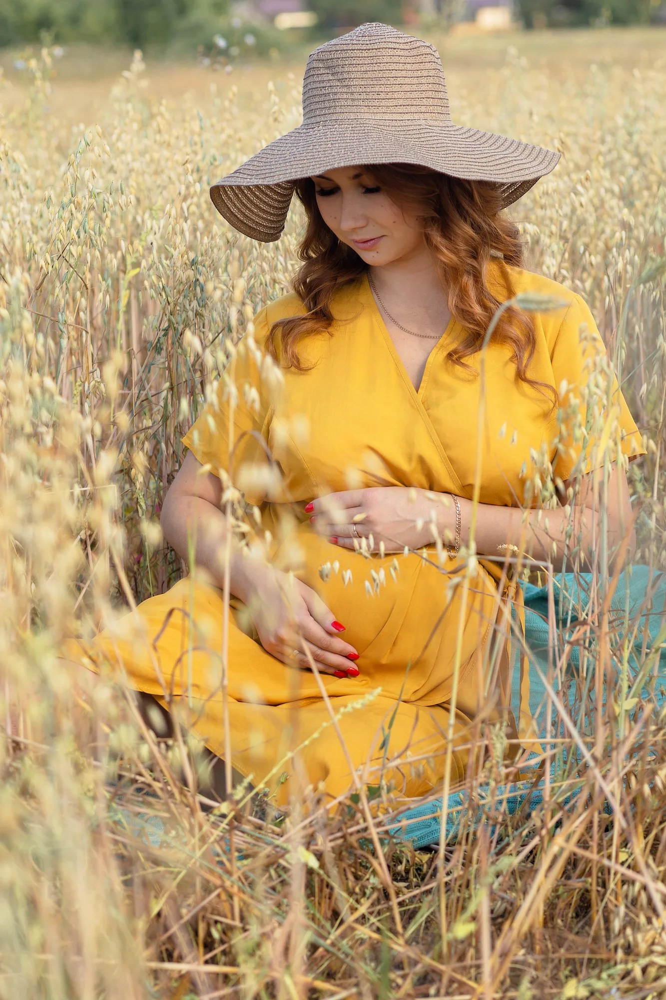 A young beautiful pregnant woman in a yellow dress and hat walks through a wheat orange field on a sunny summer day