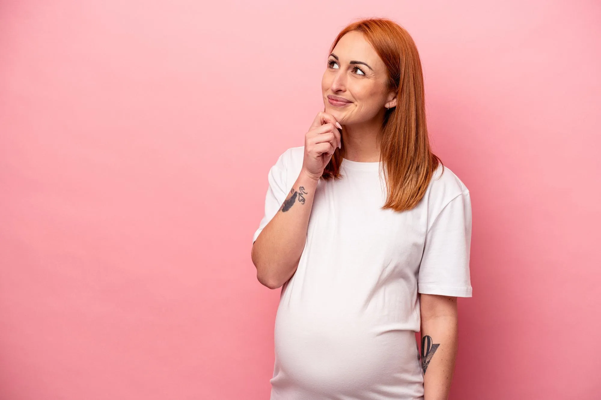 Young caucasian pregnant woman isolated on pink background looking sideways with doubtful and skeptical expression.