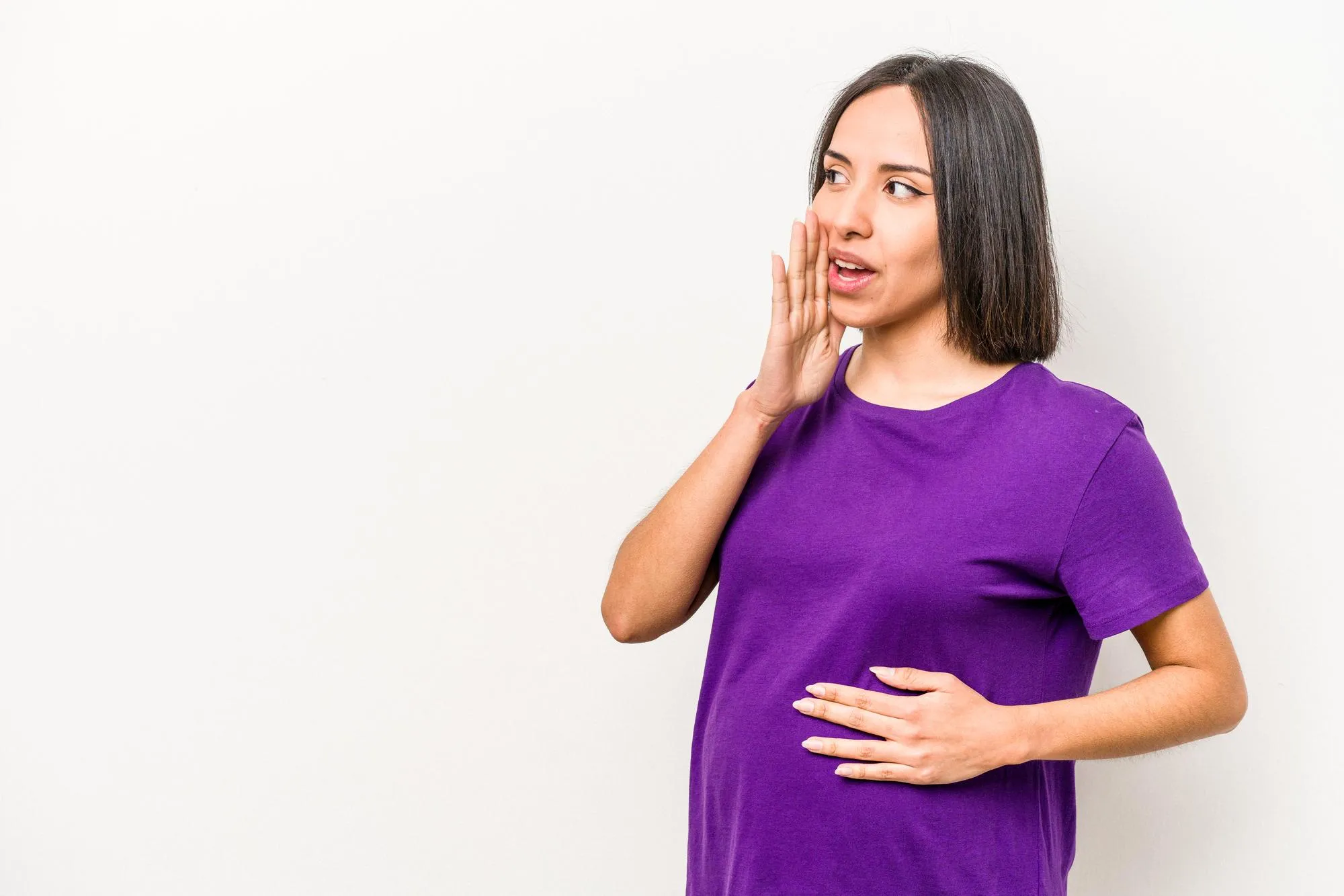 Young hispanic pregnant woman isolated on white background is saying a secret hot braking news and looking aside