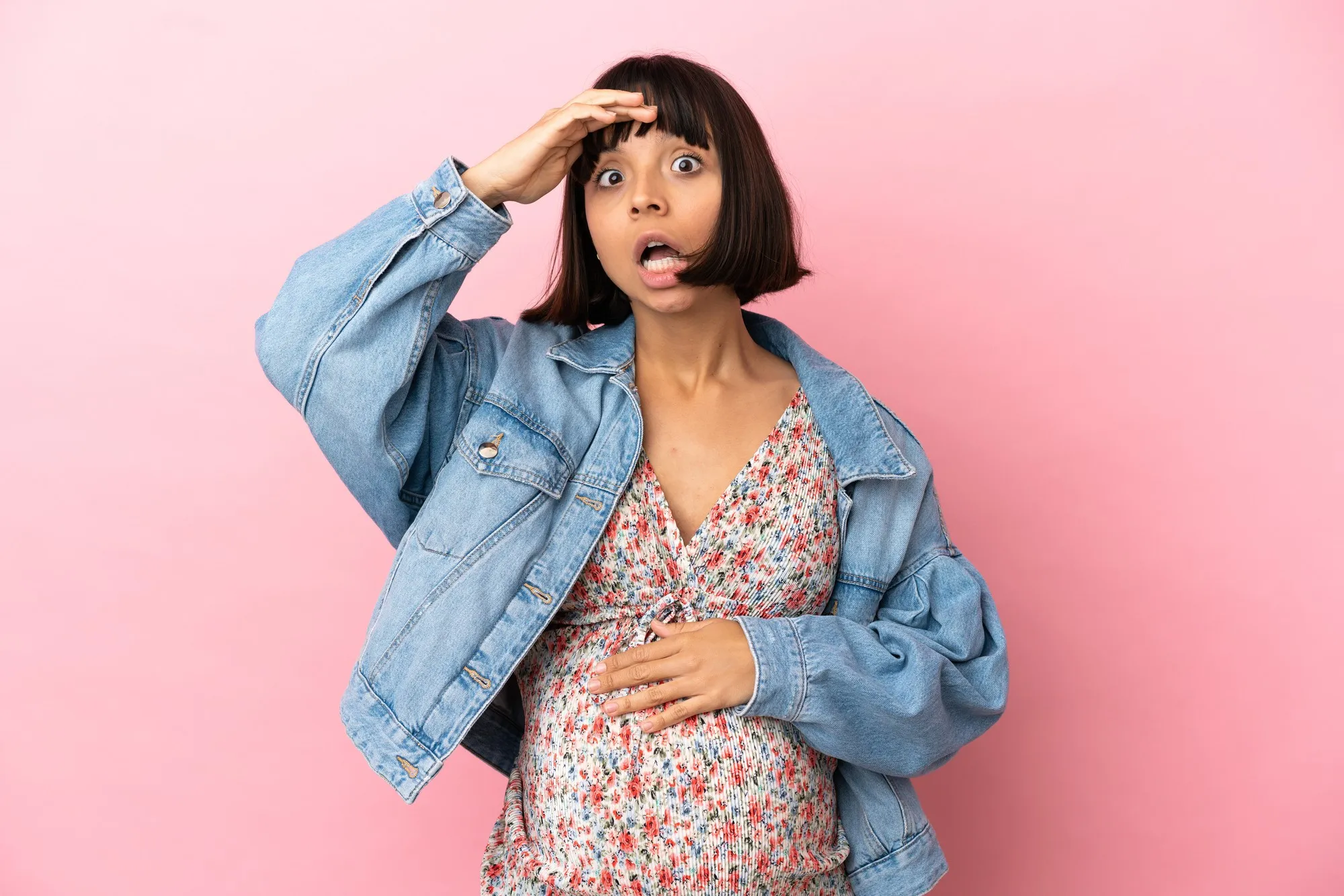 Young pregnant woman over isolated pink wall doing surprise gesture while looking to the side
