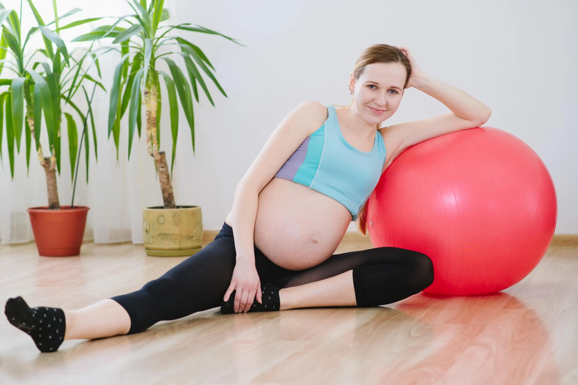 Young and pregnant woman in sportsuit doing excercises with a big ball at home