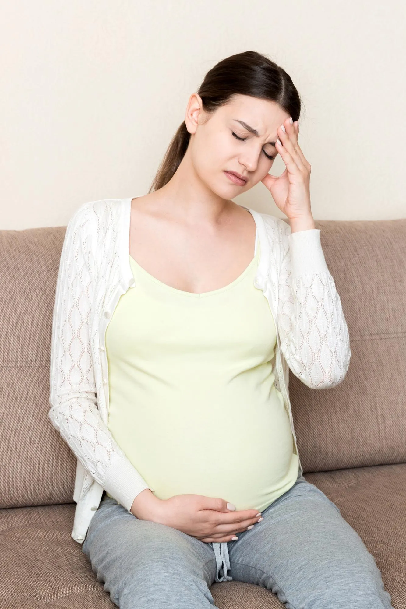 Young pregnant woman with headache sitting on sofa Pregnancy expectation concept