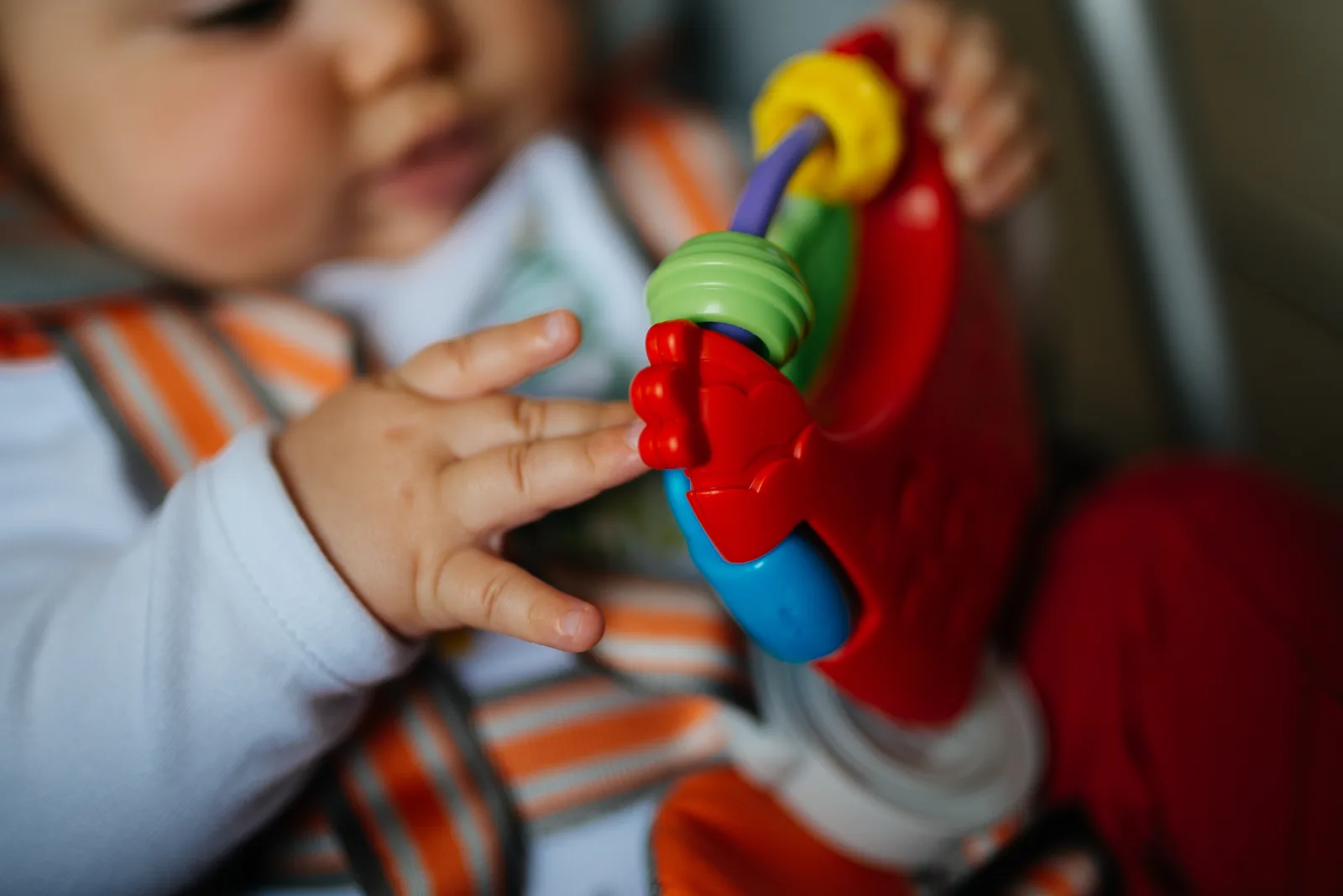 A young child engages with a vibrant, multi-colored toy while sitting securely in a high chair. The infant is focused on the toy, using their hand to explore its shapes and textures.