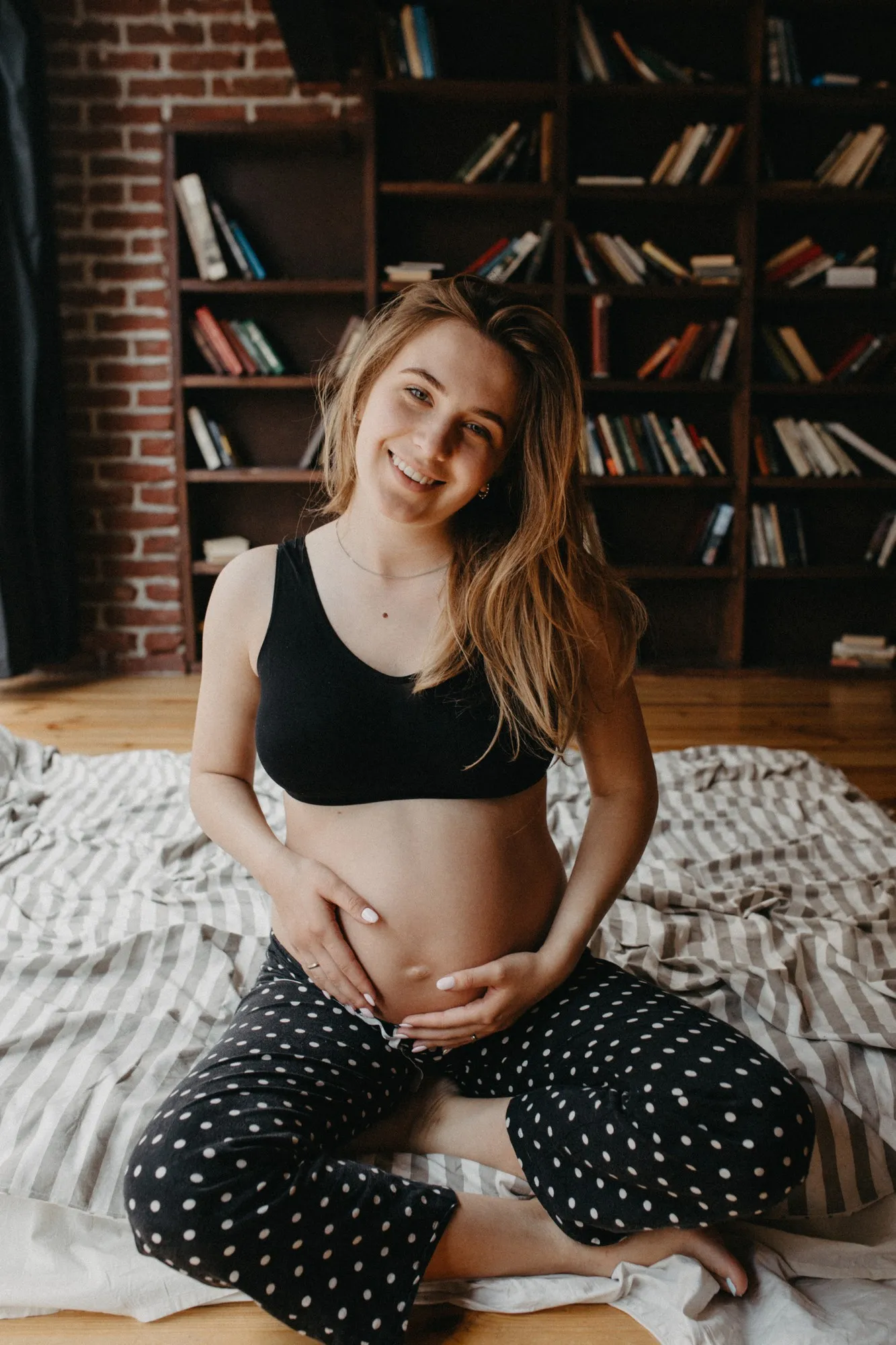 Attractive pregnant woman is sitting in bed and holding her belly Last months of pregnancy