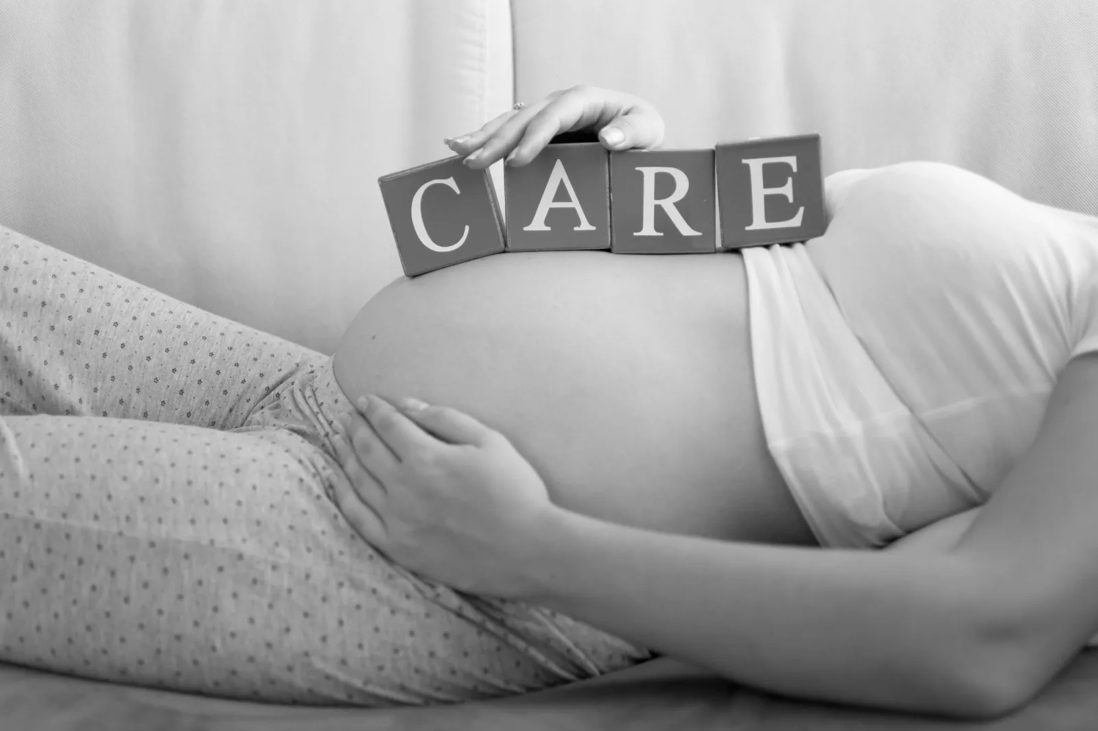 Black and white image of letters on wooden blocks making word Care on pregnant women tummy
