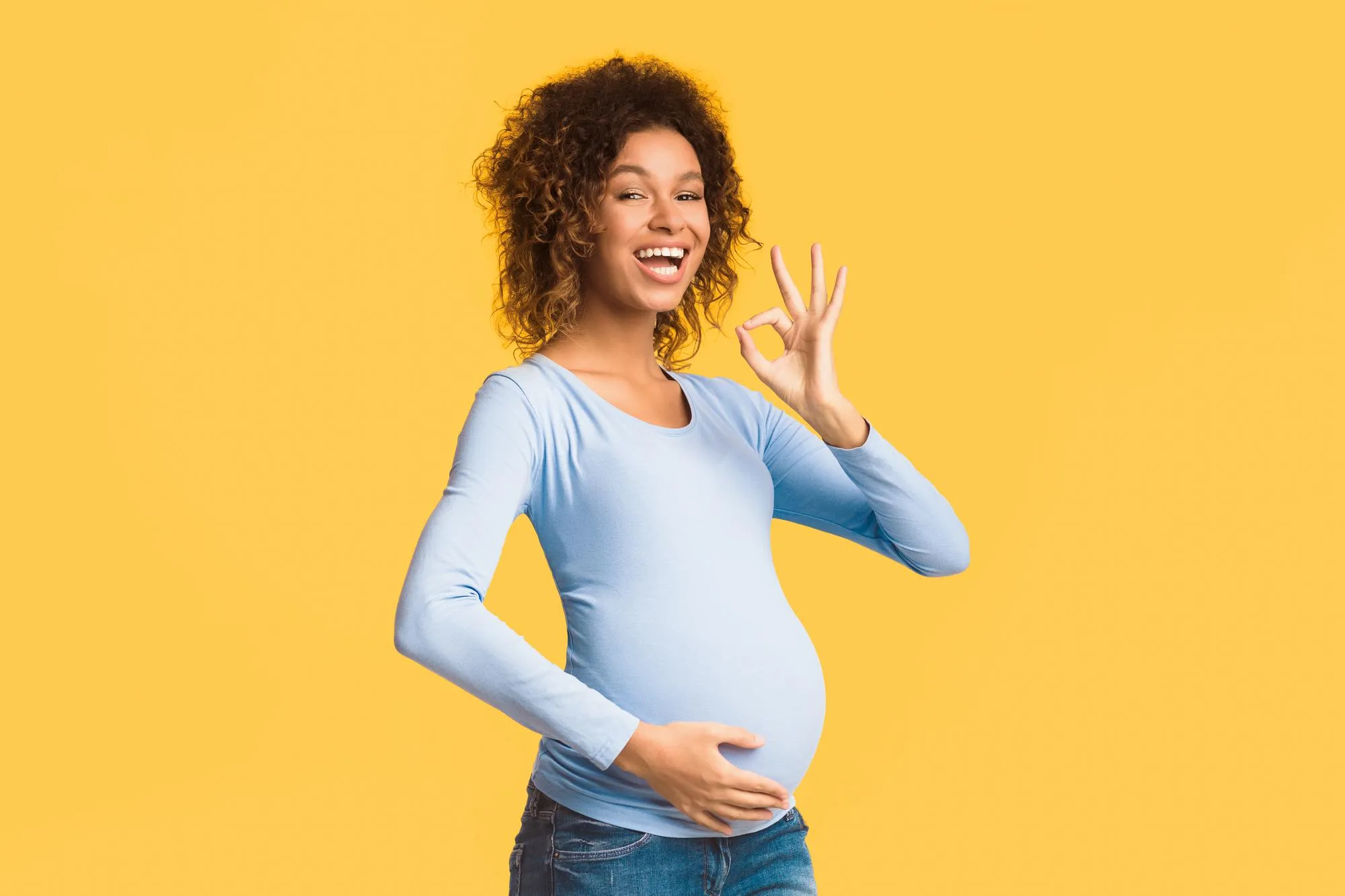 Excited afro pregnant woman showing OK gesture