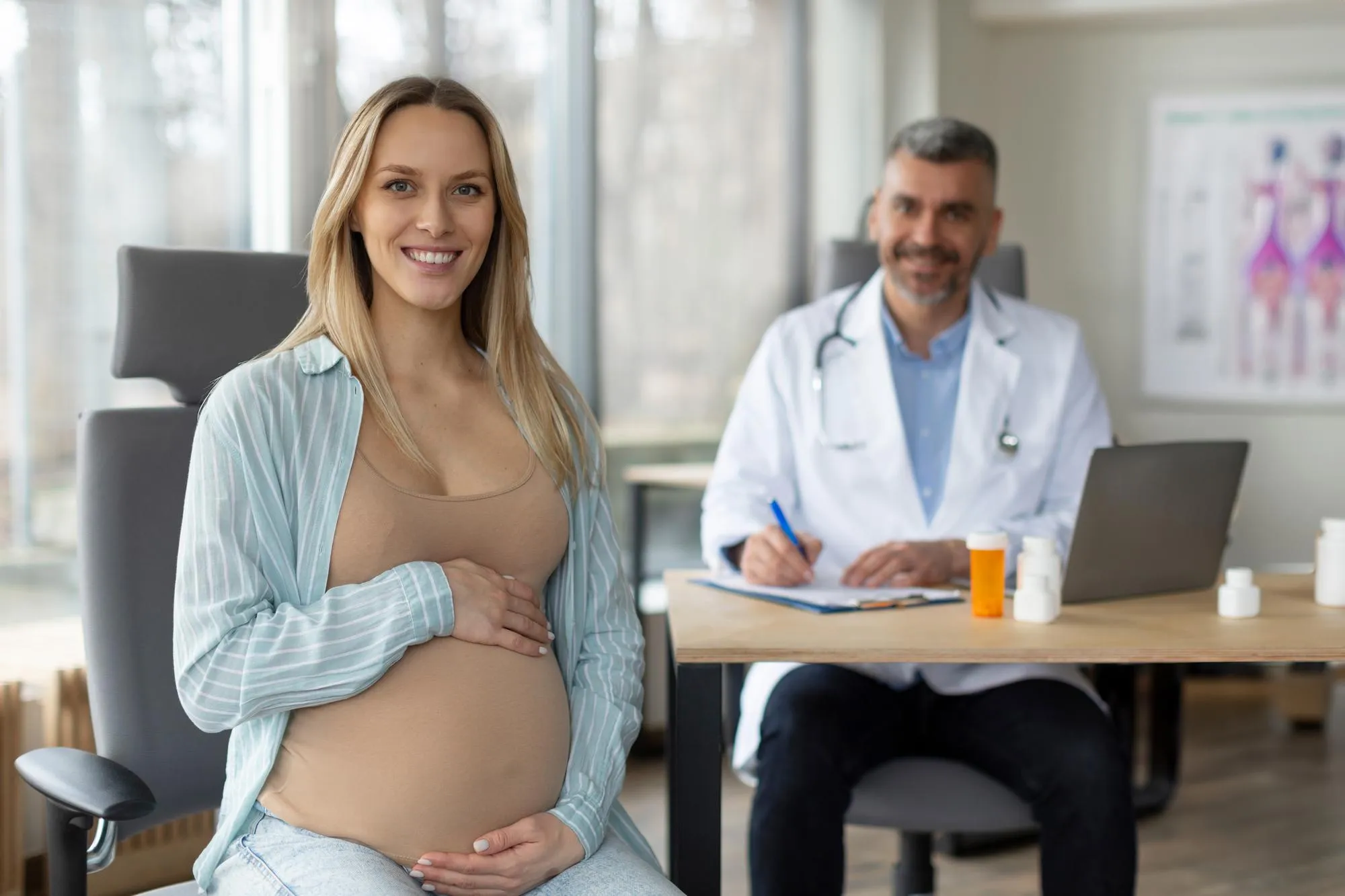 Happy young european pregnant woman sitting at clinic during consultation with middle aged male