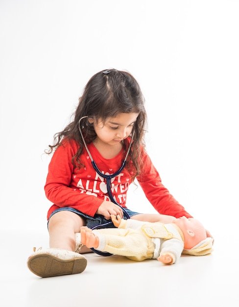 Indian Little child girl with stethoscope and Stuffed Baby or Puppy toy sitting against white background