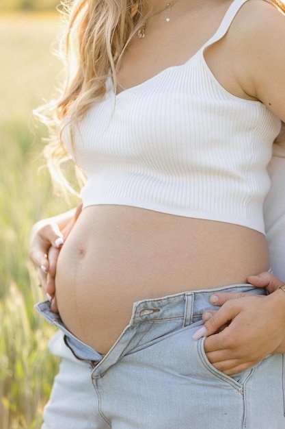 A man and a pregnant woman are jointly holding her stomach in a field