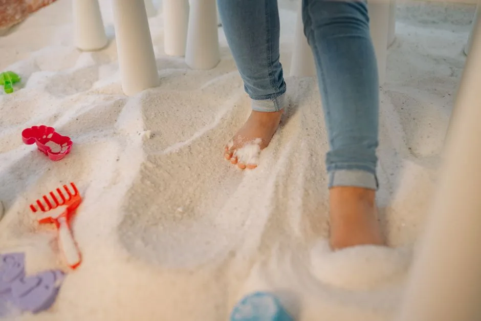 A child enjoying an indoor sand play area, standing barefoot among colorful toys.