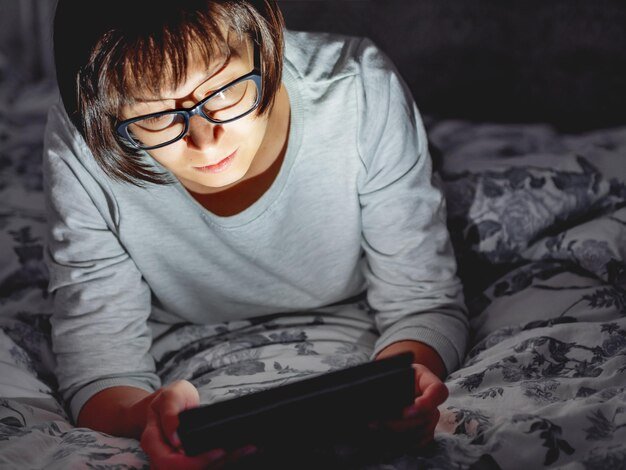 Woman in glasses are lying in bed with tablet in dark room she is touching screen night bedtime