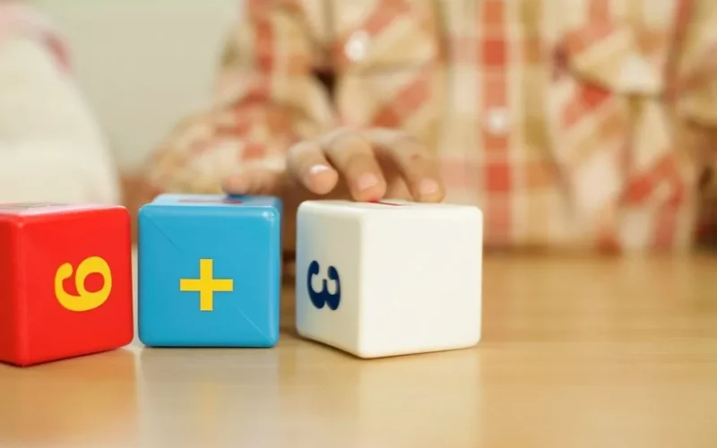Close-up of child's hand touching educational math blocks on desk.