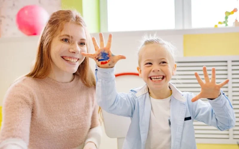A smiling child and adult enjoying painting activities indoors, showcasing joy and creativity.
