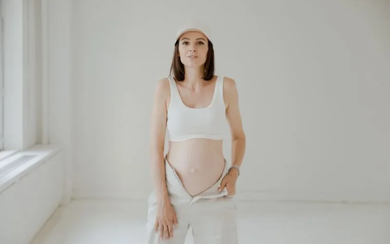 Pregnant woman in white clothing posing indoors with a serene expression.