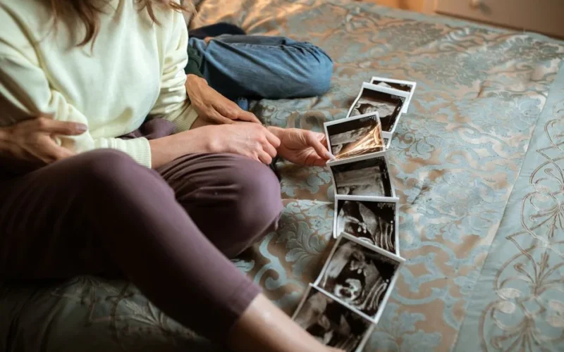 Expectant parents sit on a bed sharing ultrasound photos, symbolizing family love and anticipation.
