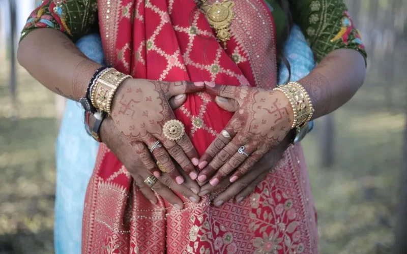 Pregnant woman in sari with intricate henna and jewelry, celebrated in nature.