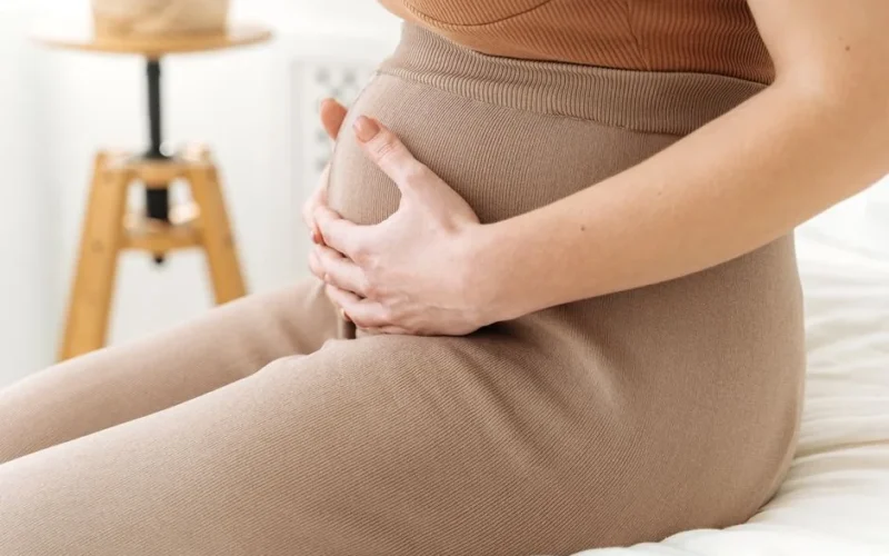 A serene close-up of a pregnant woman gently holding her belly, captured in soft natural light.