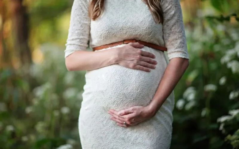 A pregnant woman in a lace dress gently cradling her belly in an outdoor setting.