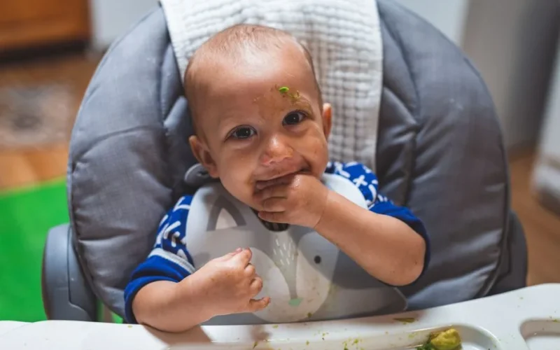 Cute baby enjoying a messy breakfast with avocado. Perfect moment of childhood captured.