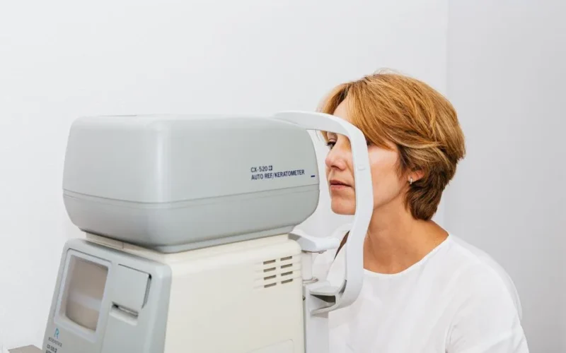 A woman undergoes an eye examination using an autorefractor machine in a clinic.