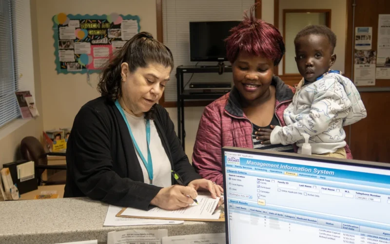 WIC staff helps WIC parent and child fill out paperwork at counter in WIC clinic in Seattle, WA. (September 2024).