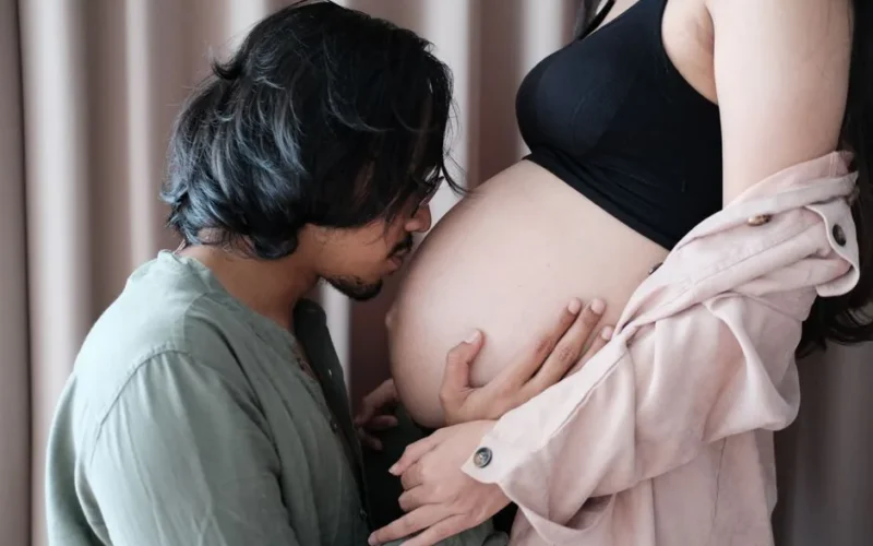 A tender moment of a couple embracing pregnancy, with a man kissing the woman's belly.