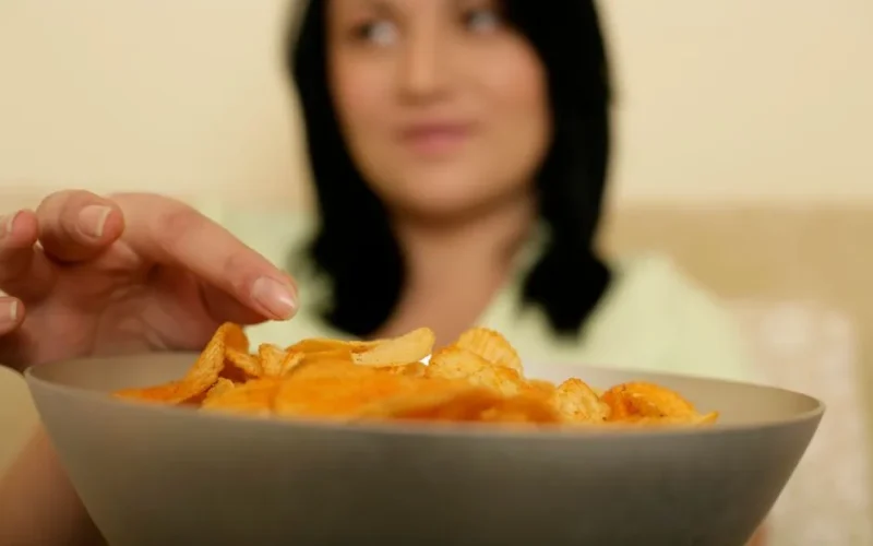 A woman reaching for a bowl full of crispy potato chips, capturing a moment of indulgence.