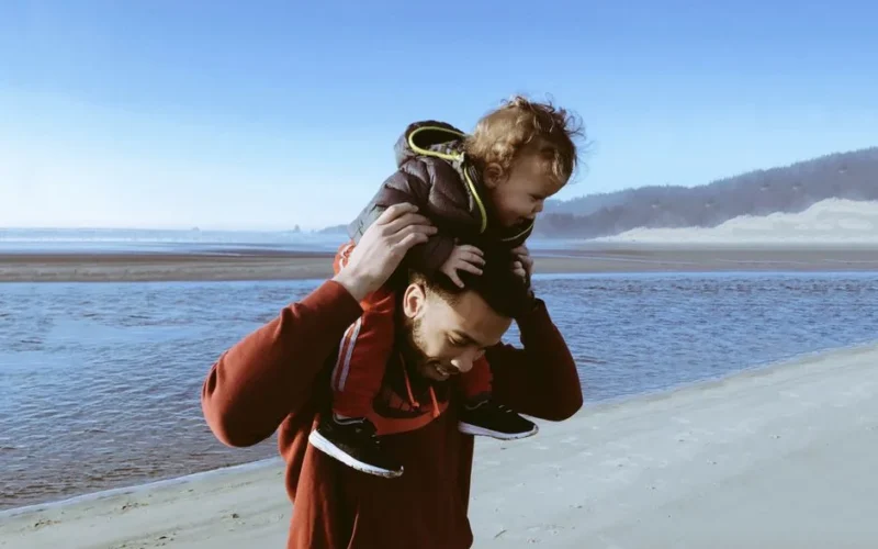 A joyful father and child bonding while walking along a sunny beach, capturing a playful moment.