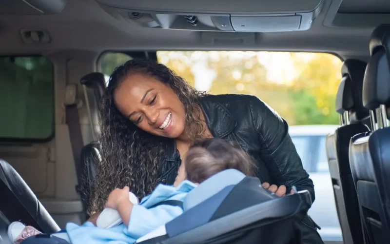 A joyful mother smiles at her baby in a car seat inside a vehicle.