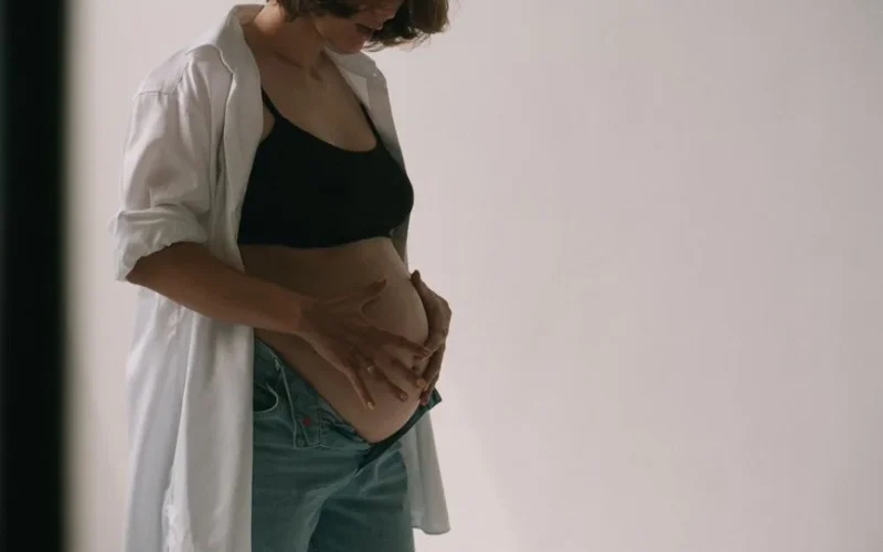 A pregnant woman in casual attire gently embraces her belly, highlighting the beauty of maternity.