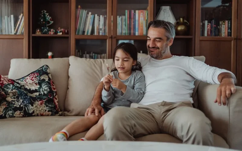 A father and daughter enjoy quality time together on a cozy couch in a warm and inviting living room.