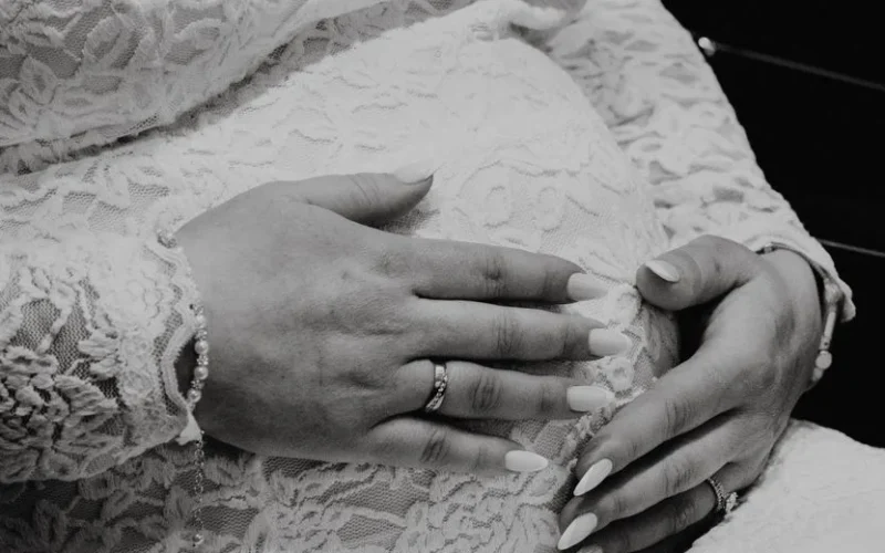 Black and white photo of a pregnant woman in lace, hands on belly.