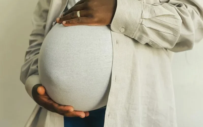 Pregnant woman in casual attire gently holding her belly, symbolizing motherhood.