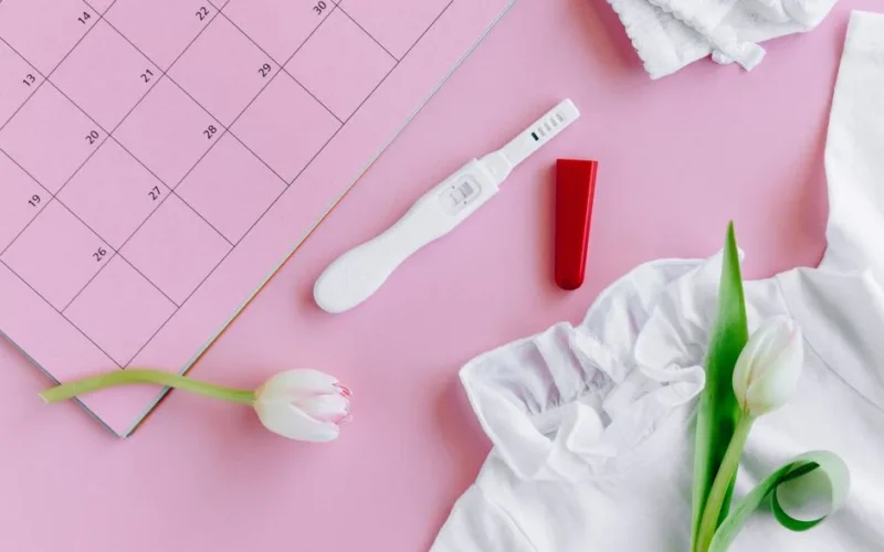 Flat lay of a pregnancy test with tulips on a pink calendar surface, symbolizing fertility and new life.