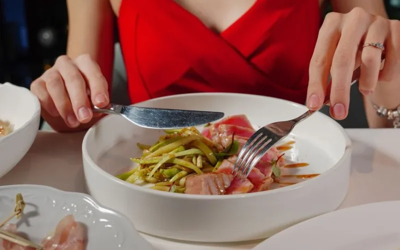 Woman in red dress enjoying a gourmet tuna and asparagus meal. Perfect for culinary and lifestyle themes.