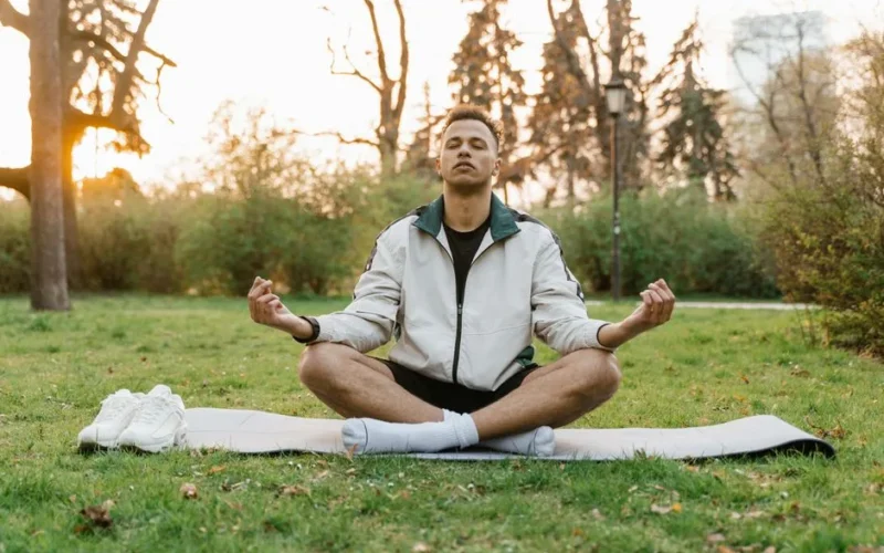 Man meditating outdoors in a tranquil park setting at sunset, promoting relaxation and mindfulness.
