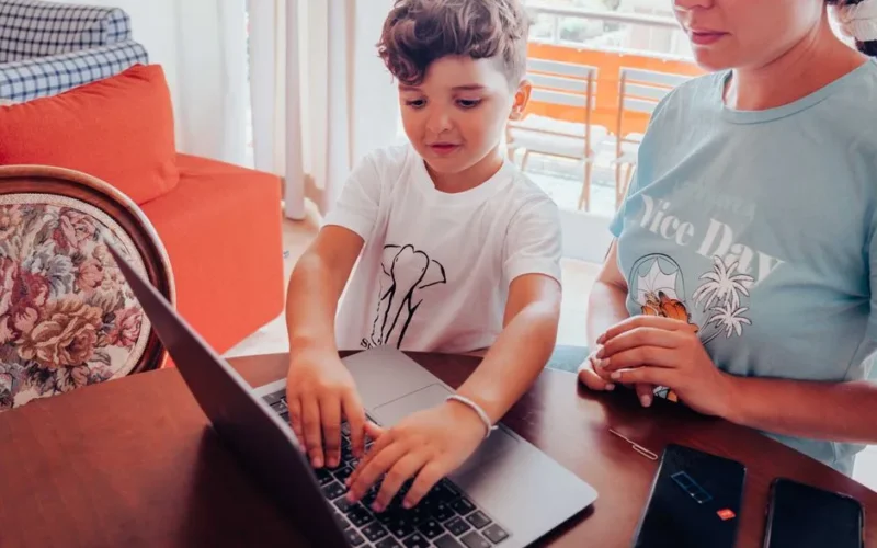 A child and mother engaging with a laptop at a home table, focused on learning or work.
