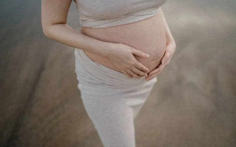 A pregnant woman gently holds her belly while standing outdoors, conveying warmth and serenity.