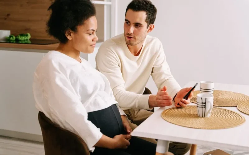 An interracial couple having a discussion about pregnancy while sitting at a kitchen table.