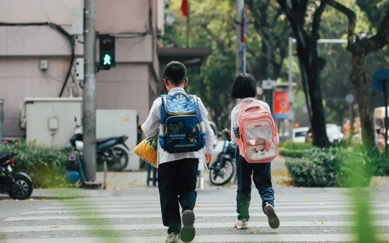 Two children with backpacks crossing a street at a pedestrian crossing.