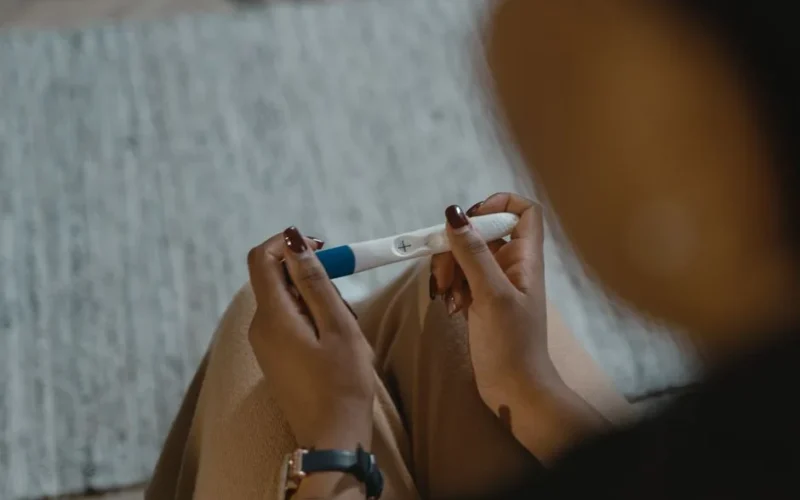 Close-up of a woman holding a positive pregnancy test with a plus sign, symbolizing new beginnings.
