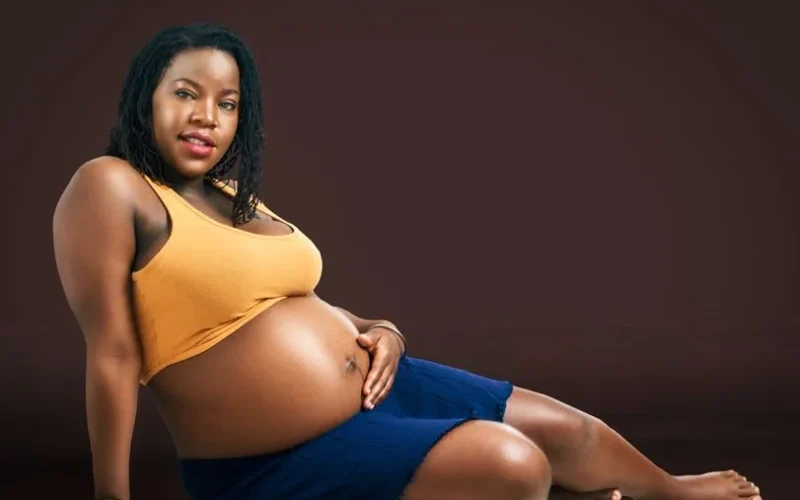 Portrait of a pregnant woman sitting in a studio with a warm smile.