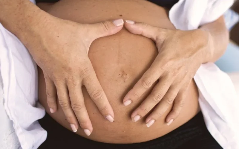 Close-up of a pregnant belly with hands forming a heart shape, symbolizing love and motherhood.